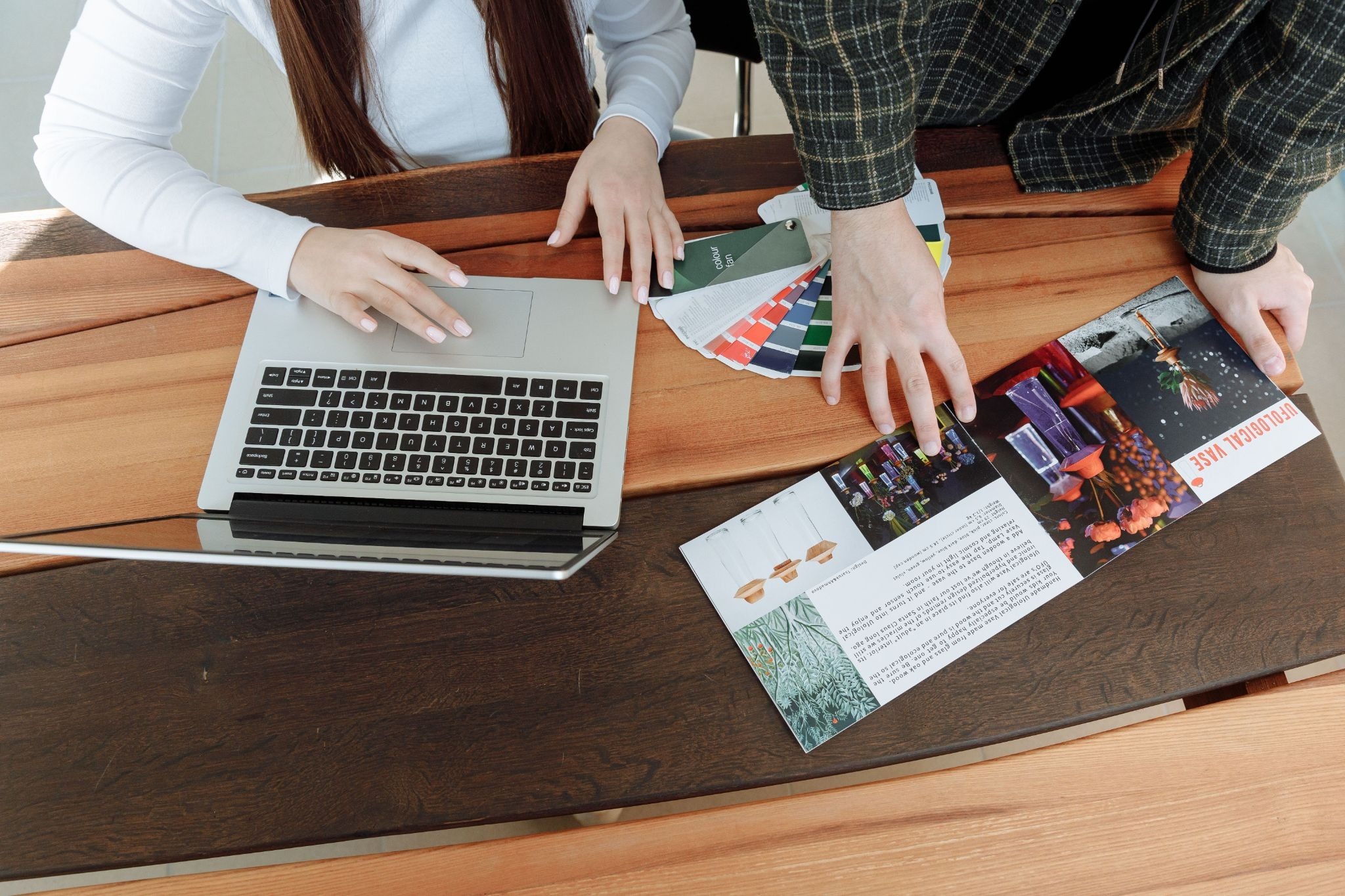 Two marketing professionals reviewing printed brochure and colour swatches at desk with laptop — print marketing campaign planning by Print It ZA