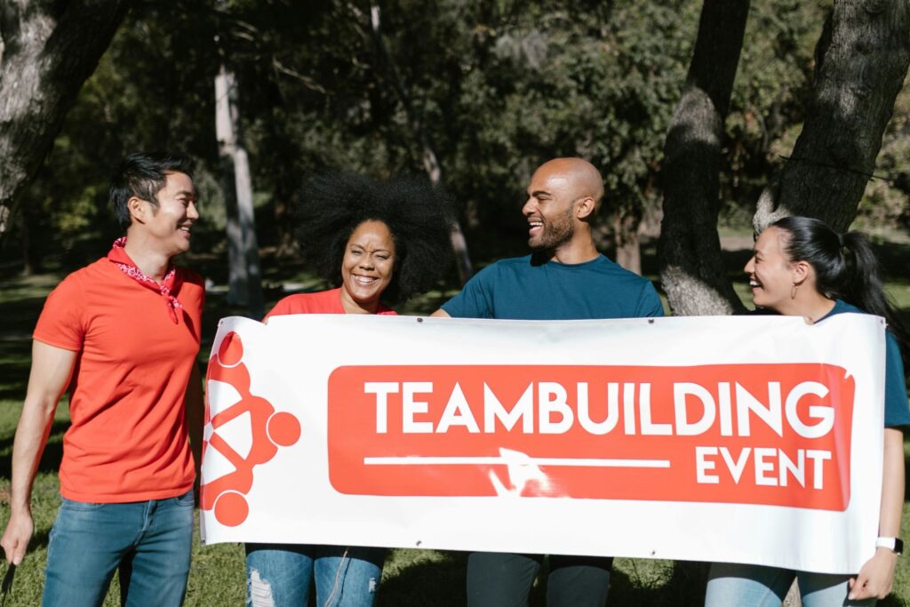 Group of four colleagues holding a printed teambuilding event banner outdoors — corporate event printing by Print It ZA